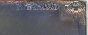 Detail view of stamps pressed into a dark grey metal plate. Letters spelling out Beard appear to have been stamped and then stamped over to the left. Another oval stamp is to our right.