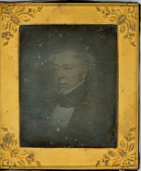 Daguerreotype. The ghostly image of a clean-shaven man with white or grey hair looks off to our left. The gold rectangular mat has leafy designs at the corners.