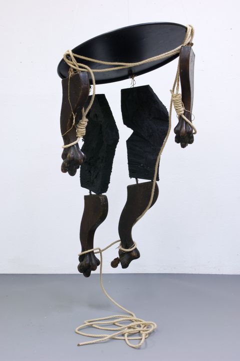 Sculpture. The round tabletop and four legs, each ending with a clawed foot, are cut apart and reassembled with wire and hung like a puppet or mobile to resemble a human body. Nooses encircle what would be the wrists, and other parts are wrapped with rope.